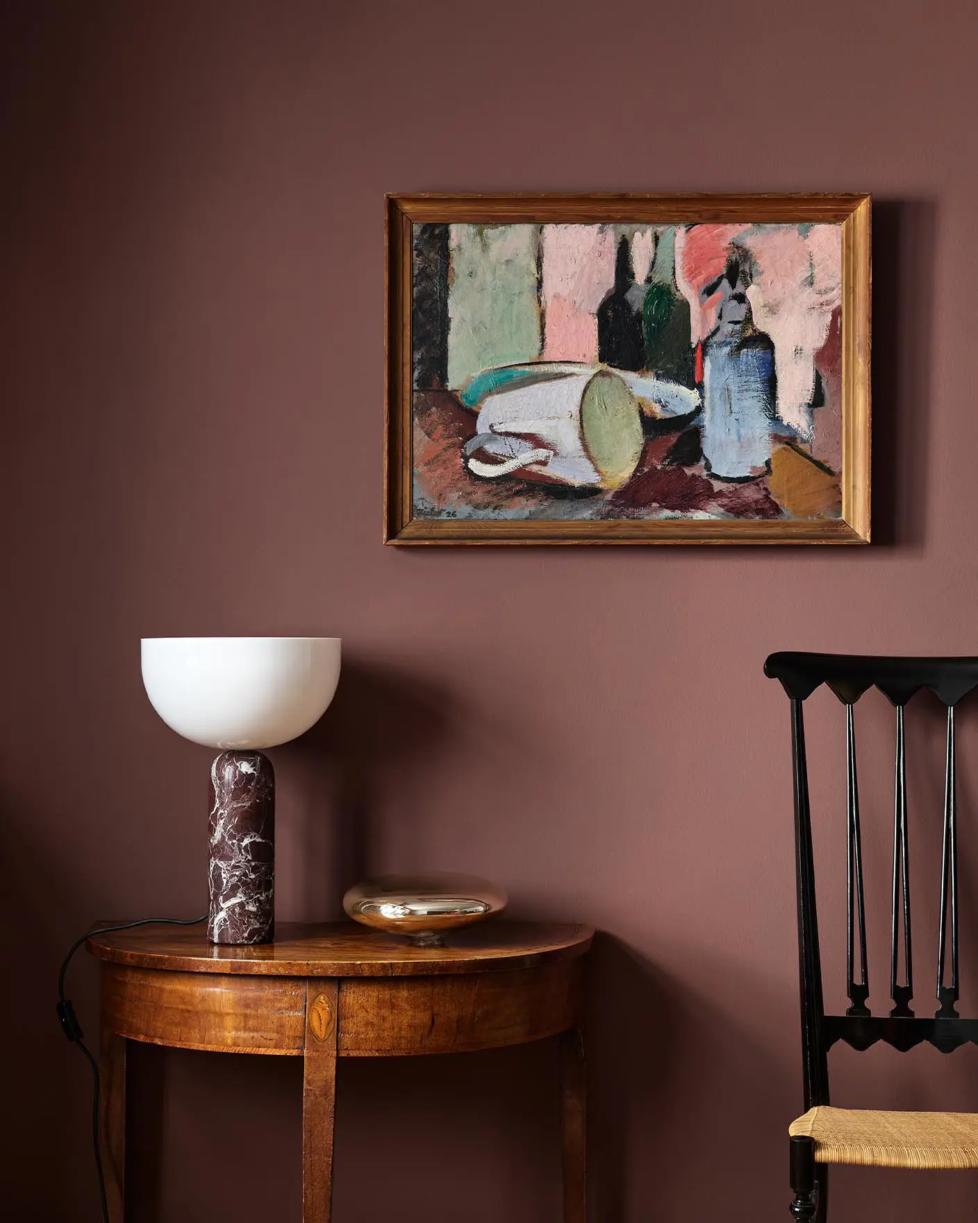 Wooden side table with a lamp beneath an abstract painting hanging on a deep red wall painted with the Jotun colour 2951 Sophisticated Red.