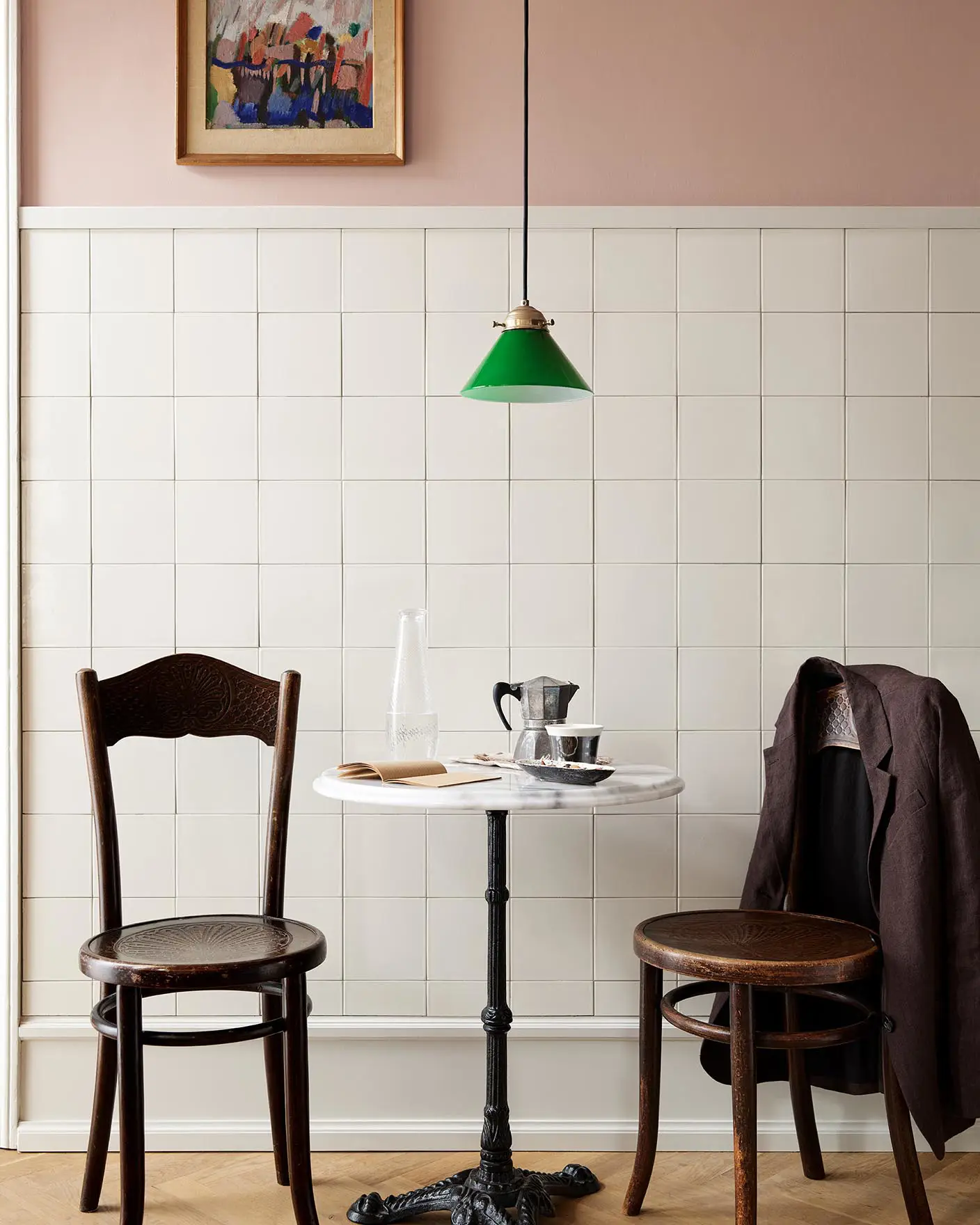 A table and wooden chairs in front of a tiled wall. The upper wall is painted in the soft pink colour Jotun 20362 Pink Ambience. 