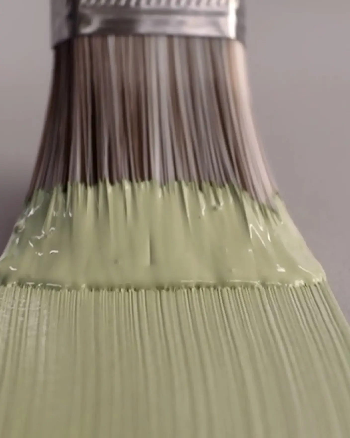 Pensel med ljusgrön färg på borsten, närbild mot grå bakgrund.