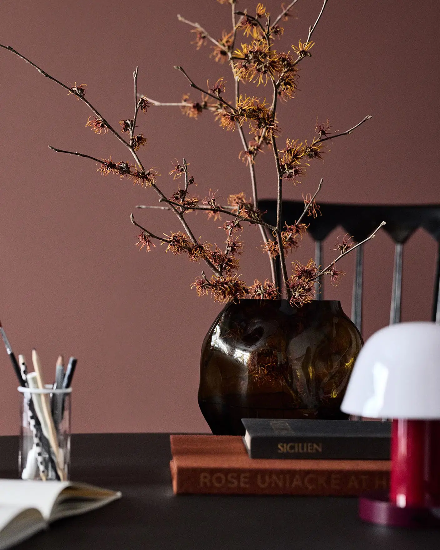 A glass vase on a table set against a deep red wall painted in the colour 2951 Sophisticated Red from Jotun.